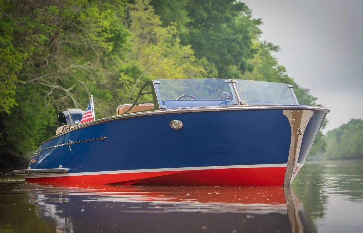 A blue and red boat with a tan interior on a wooded waterway.
