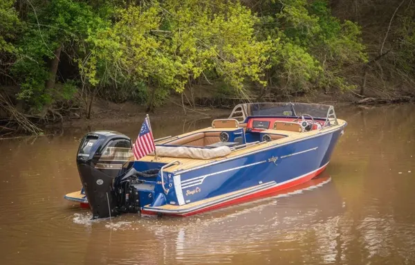 Blue boat with a tan interior on a wooded waterway.