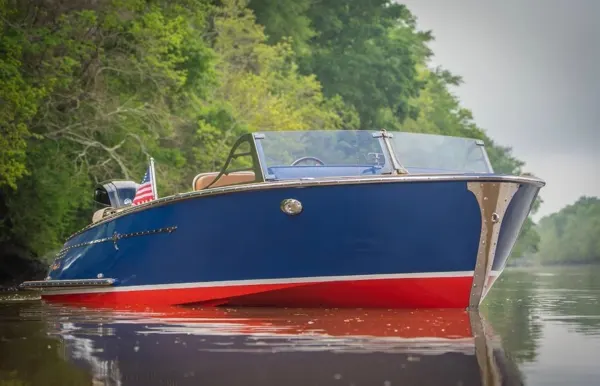 A blue and red boat with a tan interior on a wooded waterway.